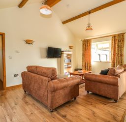 A living room with two brown sofas a wooden coffee table a wall-mounted TV and a bookshelf at Sunnyside Cottage in Blackborough End near Kings Lynn