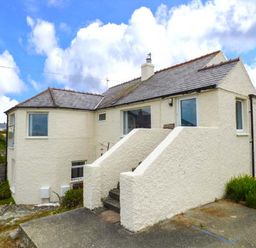 A two-story house with cream walls and slate roof with concrete steps leading to the entrance at Ty'r Enfys Bach - Upper in Trearddur Bay