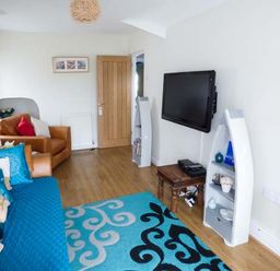 A living room with a blue patterned rug a mounted flat screen tv and brown sofas at Tyr Enfys Bach - Upper in Trearddur Bay