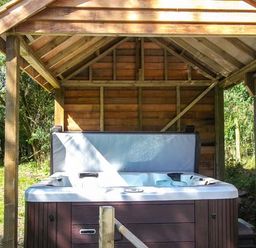 An outdoor hot tub under a wooden shelter in a garden at Ploony Cottage in Bleddfa