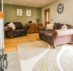 A living room with two brown sofas a wooden cabinet wall clock and a fireplace at Primrose Cottage in Aldingham