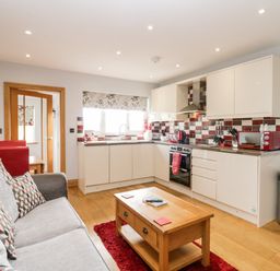 A kitchen and living area with a gray sofa a wooden coffee table and red accents at Daisy Cottage in Aldingham
