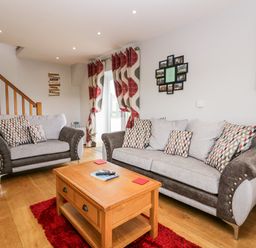 A living room with two sofas a wooden coffee table a red rug and patterned curtains at Daisy Cottage in Aldingham