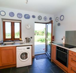 A kitchen with a washing machine, sink, and door at Pound Cottage in Huntshaw near Great Torrington