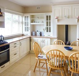 A kitchen with white cabinets wooden countertops a stove an oven a round wooden table six wooden chairs and a blue bowl on the table at Lovers Lodge in Kilkenny County Kilkenny