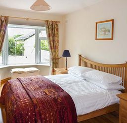 A bedroom with a wooden bed white bedding a red blanket two bedside tables with lamps and a window with curtains at Lovers Lodge in Kilkenny County Kilkenny