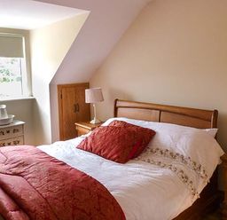 A bedroom with a wooden bed and red bedding a chest of drawers with a basin and jug two bedside tables with lamps at Lovers Lodge in Kilkenny County Kilkenny