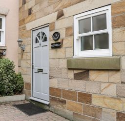 A stone exterior wall with a white door and window next to some plants at Razorbill Cottage in Whitby