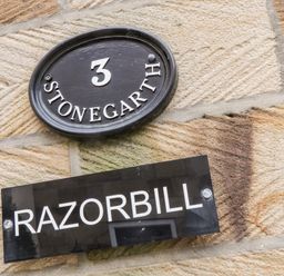 A stone wall with a black oval plaque showing number 3 and word Stonegarth and a black rectangular sign with the word Razorbill
