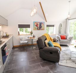 A kitchen and living area with a grey sofa, armchair, dining table, and sliding glass doors at Lands Brow Lodge in Wigton
