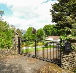 A gated entrance with stone pillars and iron gate leading to a driveway and house surrounded by trees at Treetops in Govilon near Abergavenny