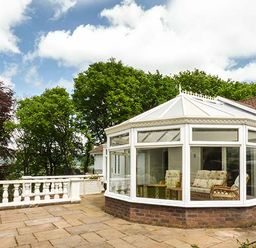 A conservatory with chairs and a table surrounded by a stone patio and trees at Treetops in Govilon near Abergavenny