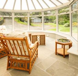 A conservatory with wicker chairs and tables overlooking a garden at Treetops in Govilon near Abergavenny