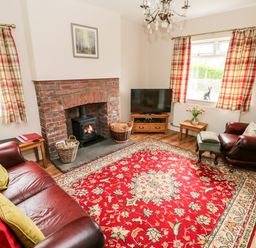 A living room with a red patterned rug a brick fireplace two leather armchairs and plaid curtains at Pondfield Gate in Cwmgors