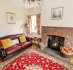 A living room with a leather sofa, wood-burning stove in a brick fireplace, and a red floral rug at Pondfield Gate in Cwmgors