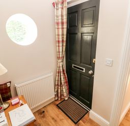 An entryway with a dark door and striped curtain next to a small wooden table with a lamp and papers at Pondfield Gate in Cwmgors