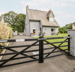 A grey house with a tiled roof behind a closed black wooden gate with a driveway and grass at Pondfield Gate in Cwmgors