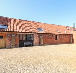 A red brick building with a tiled roof and skylights with a wooden door and a bench outside at The Long Barn in Morton on the Hill near Lenwade