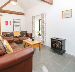 A living room with brown leather sofas a wooden coffee table a window with curtains and a black stove at The Long Barn in Morton on the Hill near Lenwade