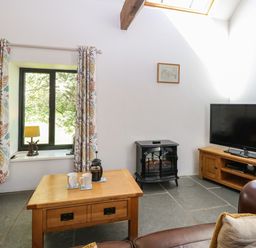 A living room with a wooden coffee table two mugs a window with patterned curtains a lamp an electric stove and a TV on a wooden stand at The Long Barn in Morton on the Hill near Lenwade