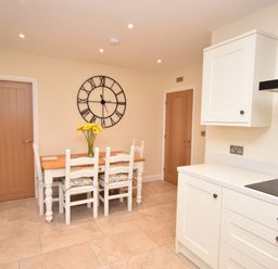 A kitchen with a wooden dining table and white chairs a large wall clock and two wooden doors at Lavender Cottage in Market Weighton