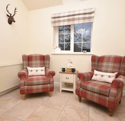 A seating area with two plaid armchairs and a small table between them under a window at Lavender Cottage in Market Weighton