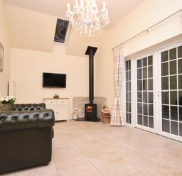 A sitting room with a leather sofa wood burning stove and glass doors with curtains at Lavender Cottage in Market Weighton