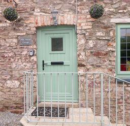 An entrance with a green door and stone wall at Milk Wood Cottage in Laugharne