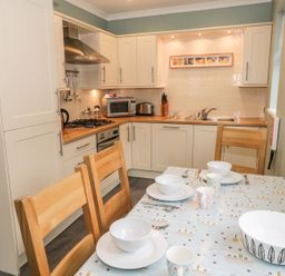 A kitchen with white cabinets wooden countertops a dining table set with bowls cups and cutlery at Thompson Cottage Ambleside
