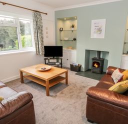 A living room with two leather sofas coffee table television and a wood-burning stove at Thompson Cottage in Ambleside