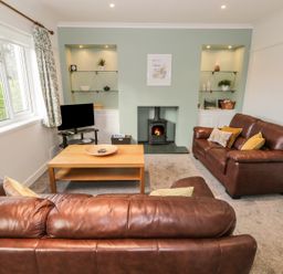 A living room with two brown leather sofas a wooden coffee table and a fireplace at Thompson Cottage in Ambleside