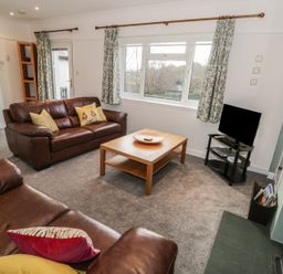 A living room with two leather sofas a wooden coffee table a television and patterned curtains at Thompson Cottage in Ambleside
