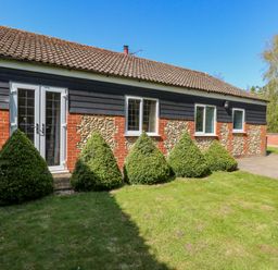 A house with a tile roof stone and brick walls and bushes in front at The Meadows Cottage in Billingford near Bawdeswell