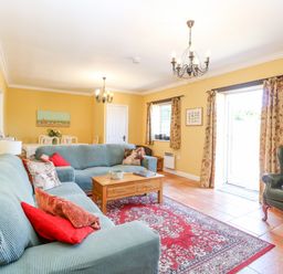 A living room with teal sofas a wooden coffee table a red patterned rug and a green armchair at The Meadows Cottage in Billingford near Bawdeswell