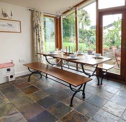 A dining area with a wooden table and benches set with dishes next to large windows overlooking a garden at Gatehouse in Painscastle