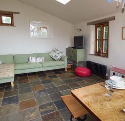 A living room with a green sofa a wooden dining table and a television on a green cabinet at Gatehouse in Painscastle
