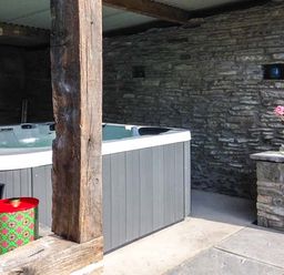 A hot tub in a stone and wood outdoor covered area with a small plant on a stone ledge at Gatehouse in Painscastle