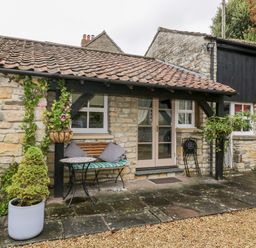 Stone cottage exterior with tiled roof bench table and potted plants at The Coach House in Bitton