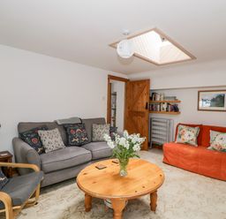 A living room with sofas armchair wooden coffee table flowers books and a skylight at The Coach House in Bitton