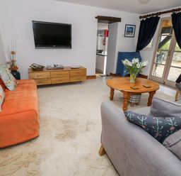 A living room with an orange sofa a gray sofa a wooden coffee table and a wall-mounted television at The Coach House in Bitton