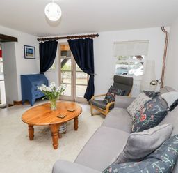 A living room with a gray sofa with cushions a wooden coffee table with flowers a gray armchair a blue chest of drawers and dark curtains at The Coach House in Bitton