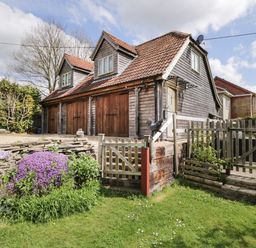 A wooden house with three garage doors surrounded by a garden with purple flowers and green grass at Shephard's Retreat in Charlton Mackrell near Somerton