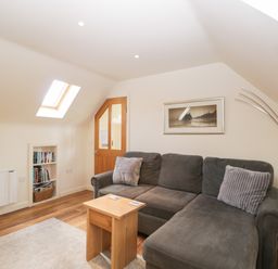 A living room with a gray sectional sofa wooden side table framed wall art bookshelf and an arched floor lamp at Shephard's Retreat in Charlton Mackrell near Somerton