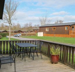 A wooden deck with a black metal table and four chairs and a potted plant overlooking a grassy area and brown wooden cabins at High Tide in Rock