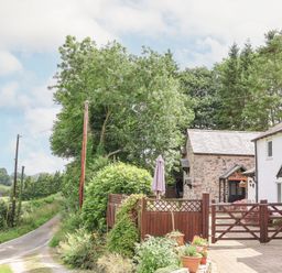 A countryside home with a stone building and wooden gate near a narrow road with trees at The Old Barn in Llanferres near Ruthin