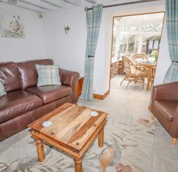 A sitting room with brown leather chairs a wooden coffee table and a view into a dining area with wicker furniture at The Old Barn in Llanferres near Ruthin