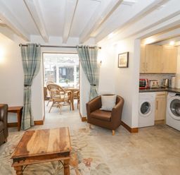 A living area with a brown leather sofa a wooden coffee table a brown armchair and kitchen appliances including a washing machine and dryer at The Old Barn in Llanferres near Ruthin
