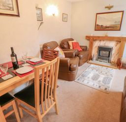A living room with a dining table set for two and leather armchairs near a fireplace at Blacksmith Cottage in Appleby-in-Westmorland