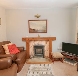 A living room with a fireplace leather sofas a small television on a stand and floral curtains at Blacksmith Cottage in Appleby-in-Westmorland