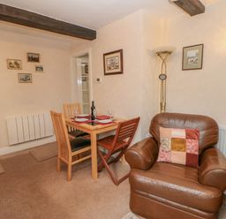 A living room with a wooden dining table set with plates and glasses and brown leather armchairs at Blacksmith Cottage in Appleby-in-Westmorland
